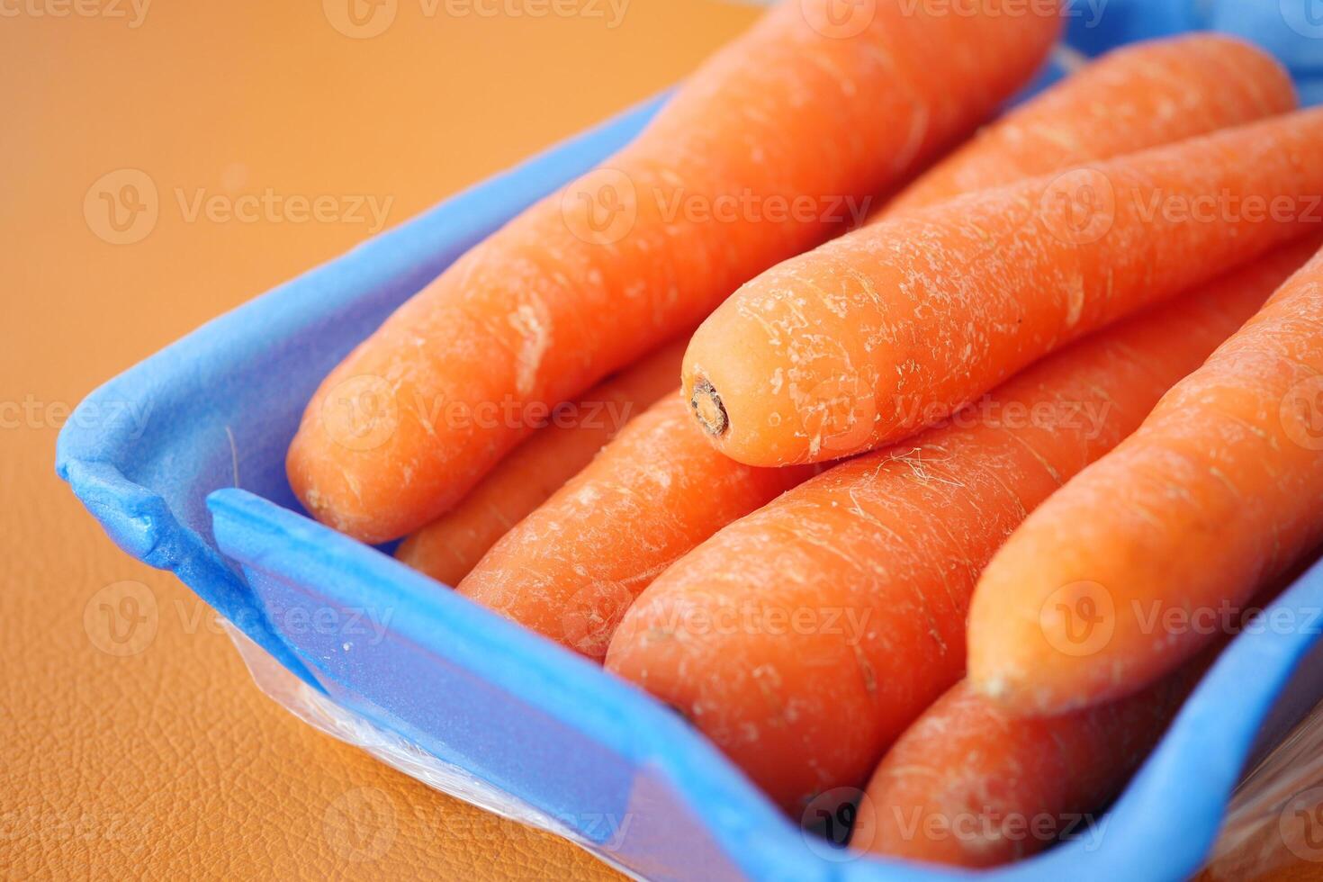 Fresh carrots displayed in a blue tray on an orange surface photo