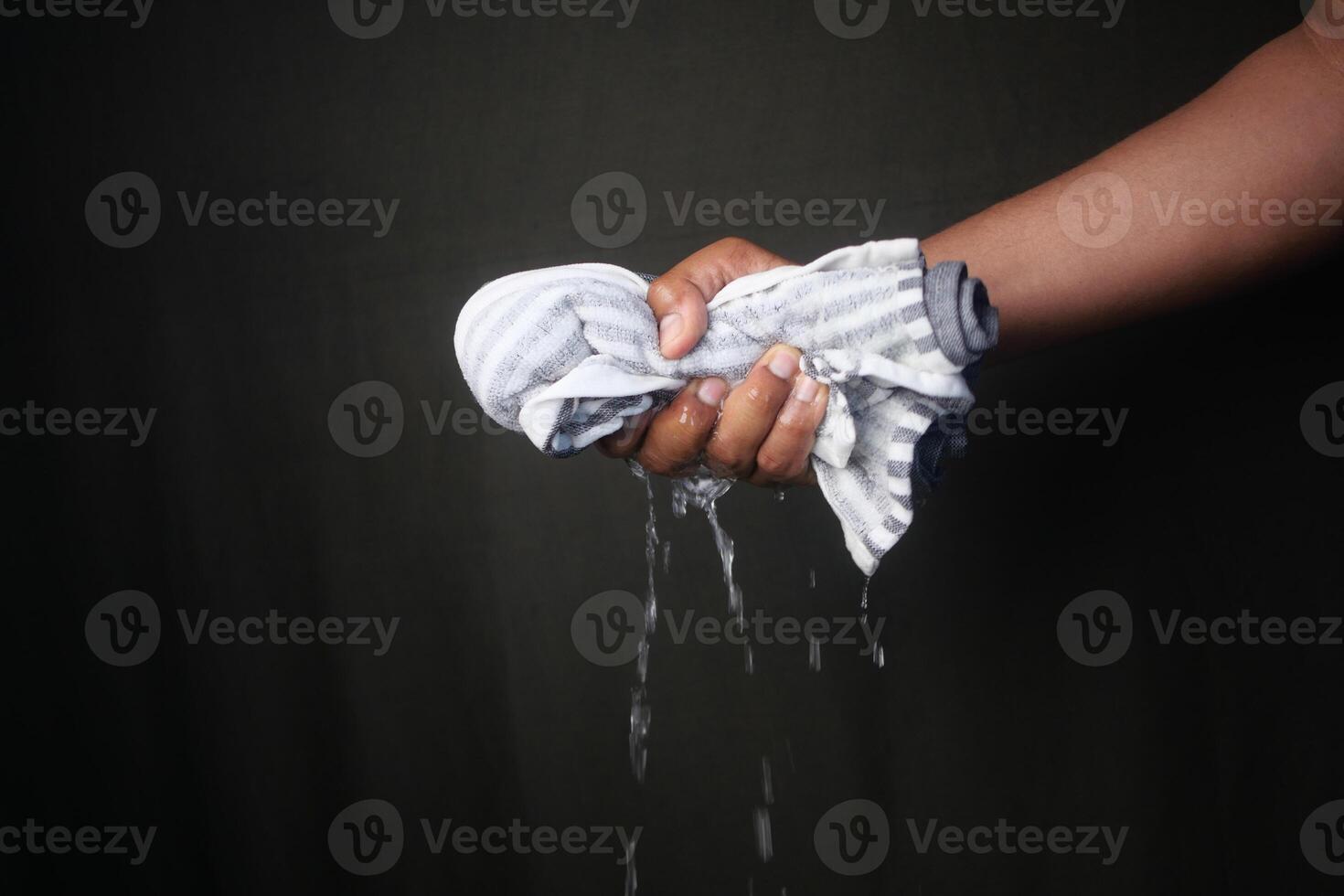 Hand squeezing a wet cloth with water dripping in low light photo