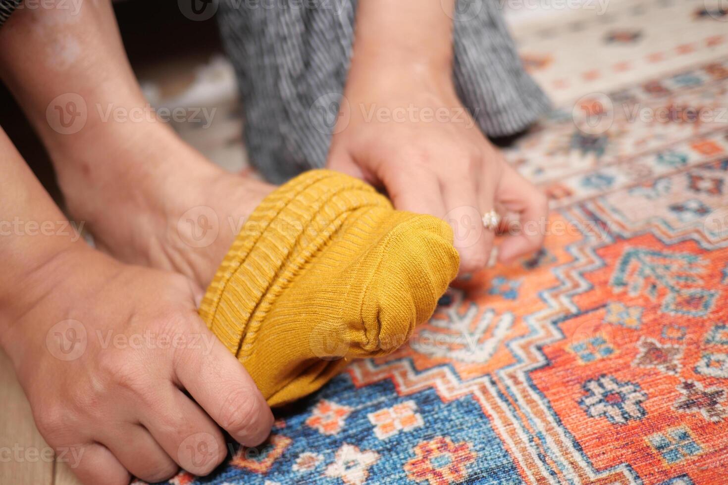 Hands pulling on a yellow sock on a colorful patterned rug photo