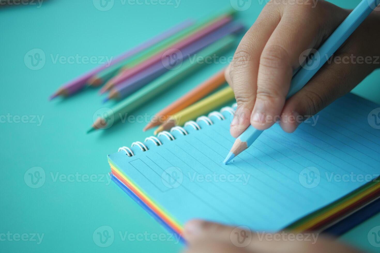 Child writing with colored pencils on a blue notepad in daylight photo