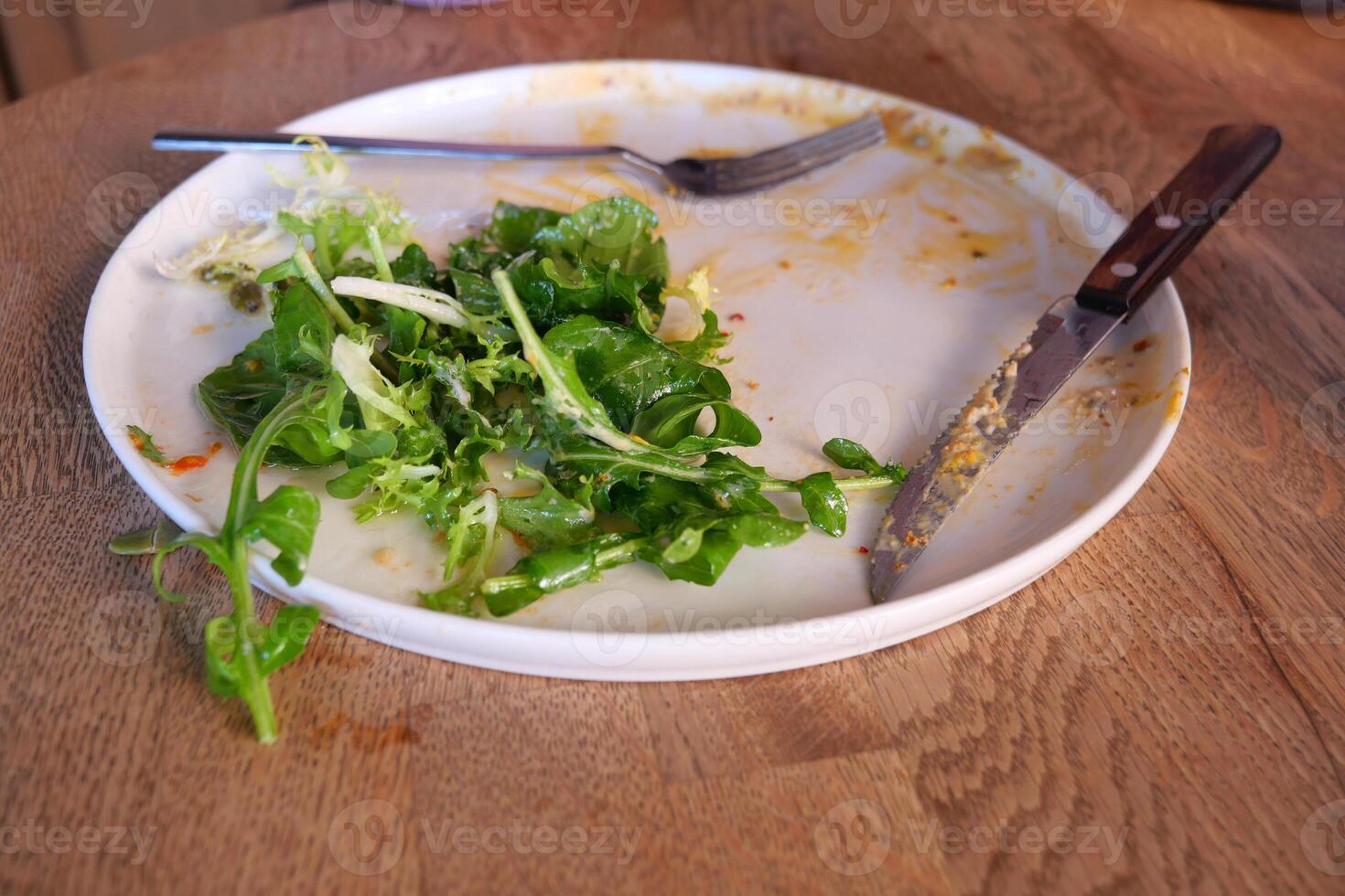 Leftover salad on a plate with utensils after meal photo