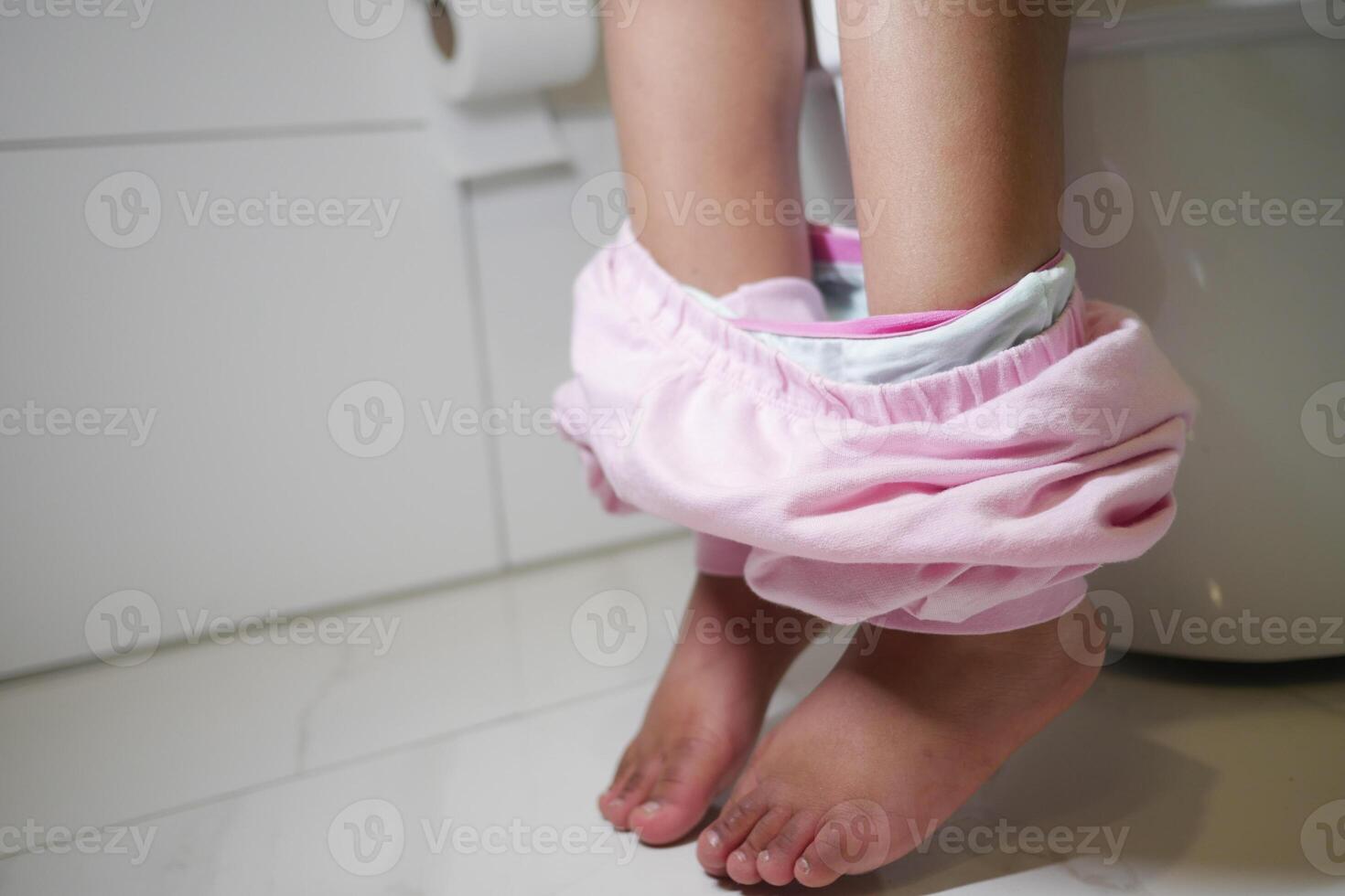 Child in pink pants using the toilet in a modern bathroom setting photo
