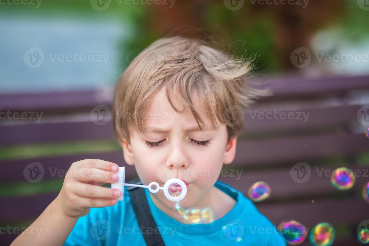 A young boy blowing soap bubbles on a bench photo