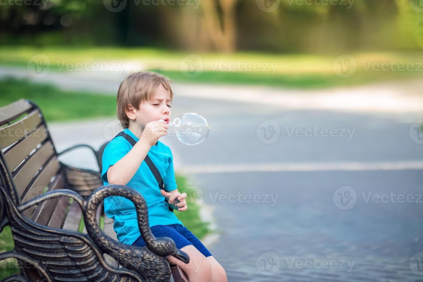 A young boy sitting on a bench blowing bubbles photo