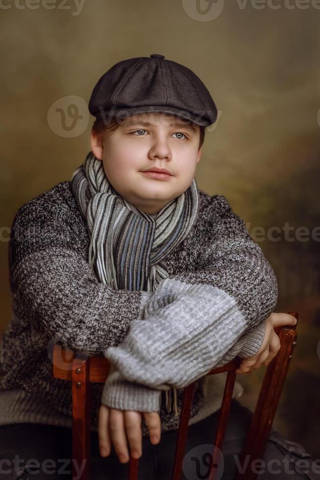 A boy wearing a hat and scarf sitting on a chair photo