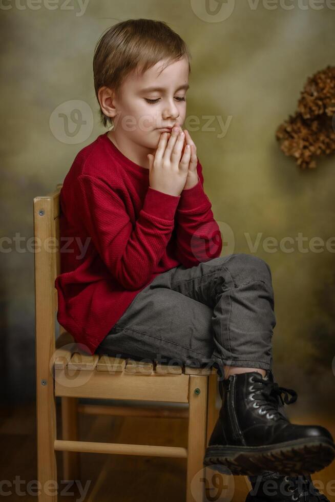 A young boy sitting on a chair with his hands folded photo