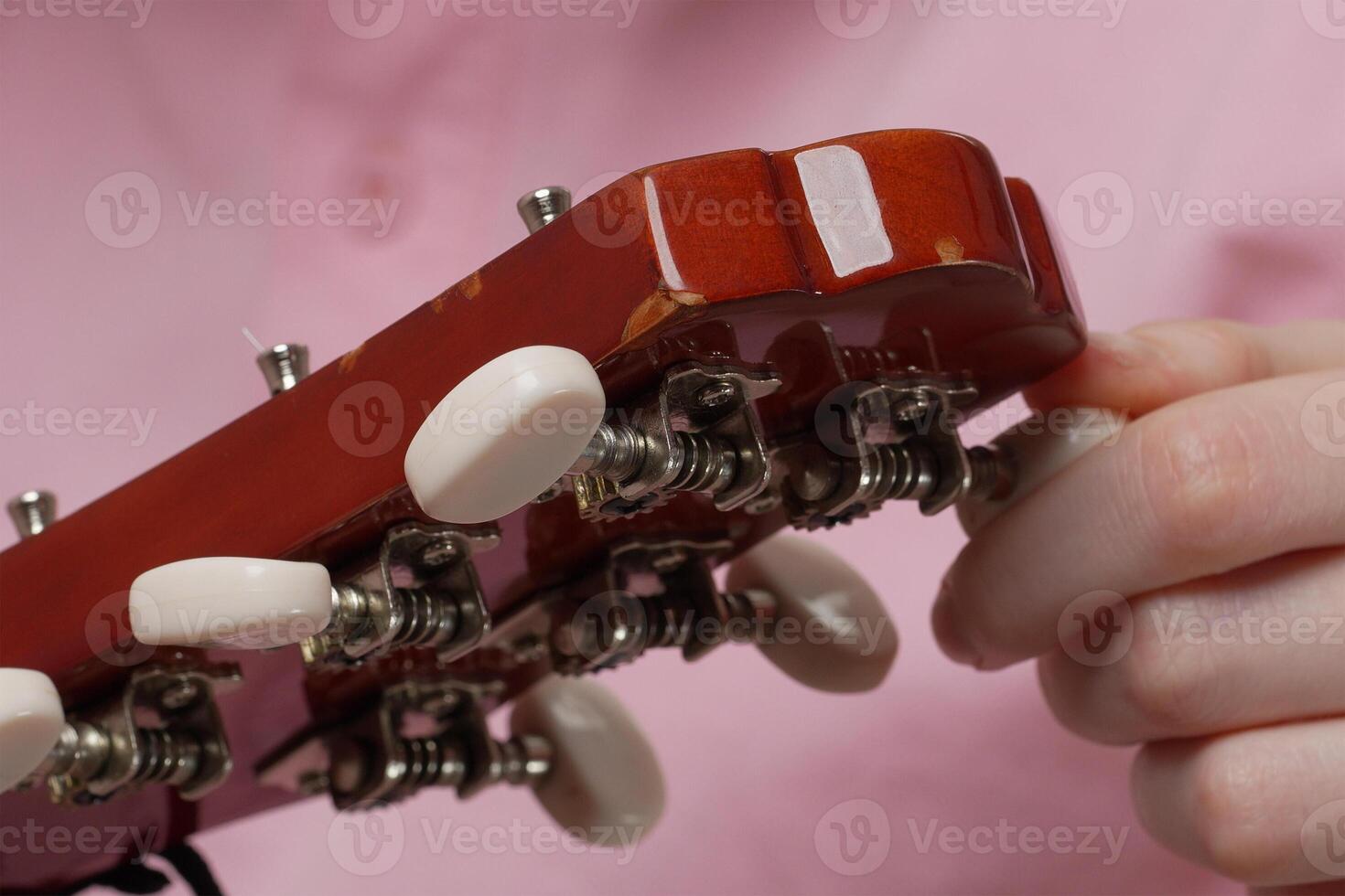 Extreme closeup of female fingers tuning acoustic guitar, tightening and loosening strings photo