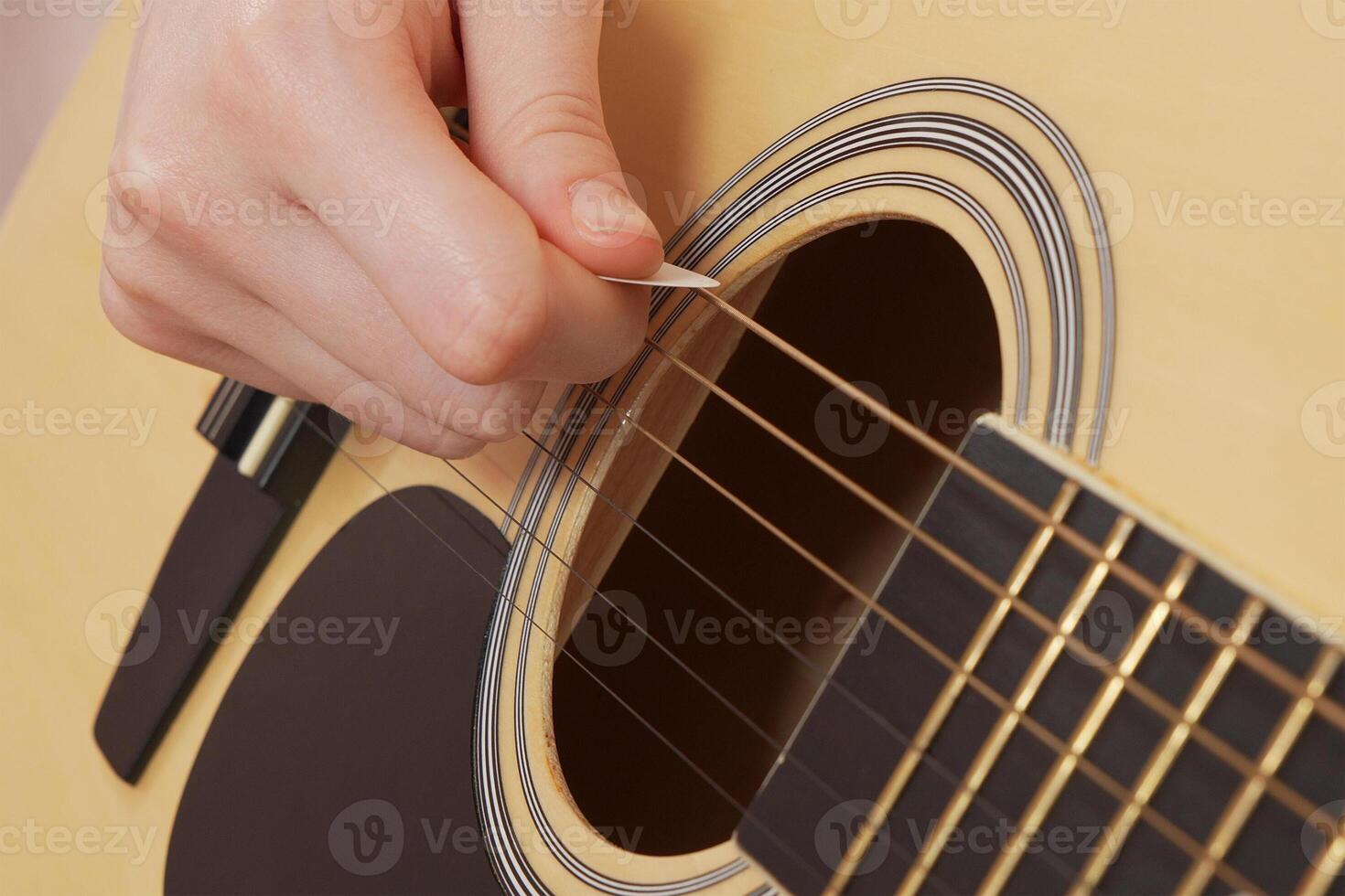 Extreme closeup woman's fingers deftly handling guitar pick as strumming six string acoustic guitar photo