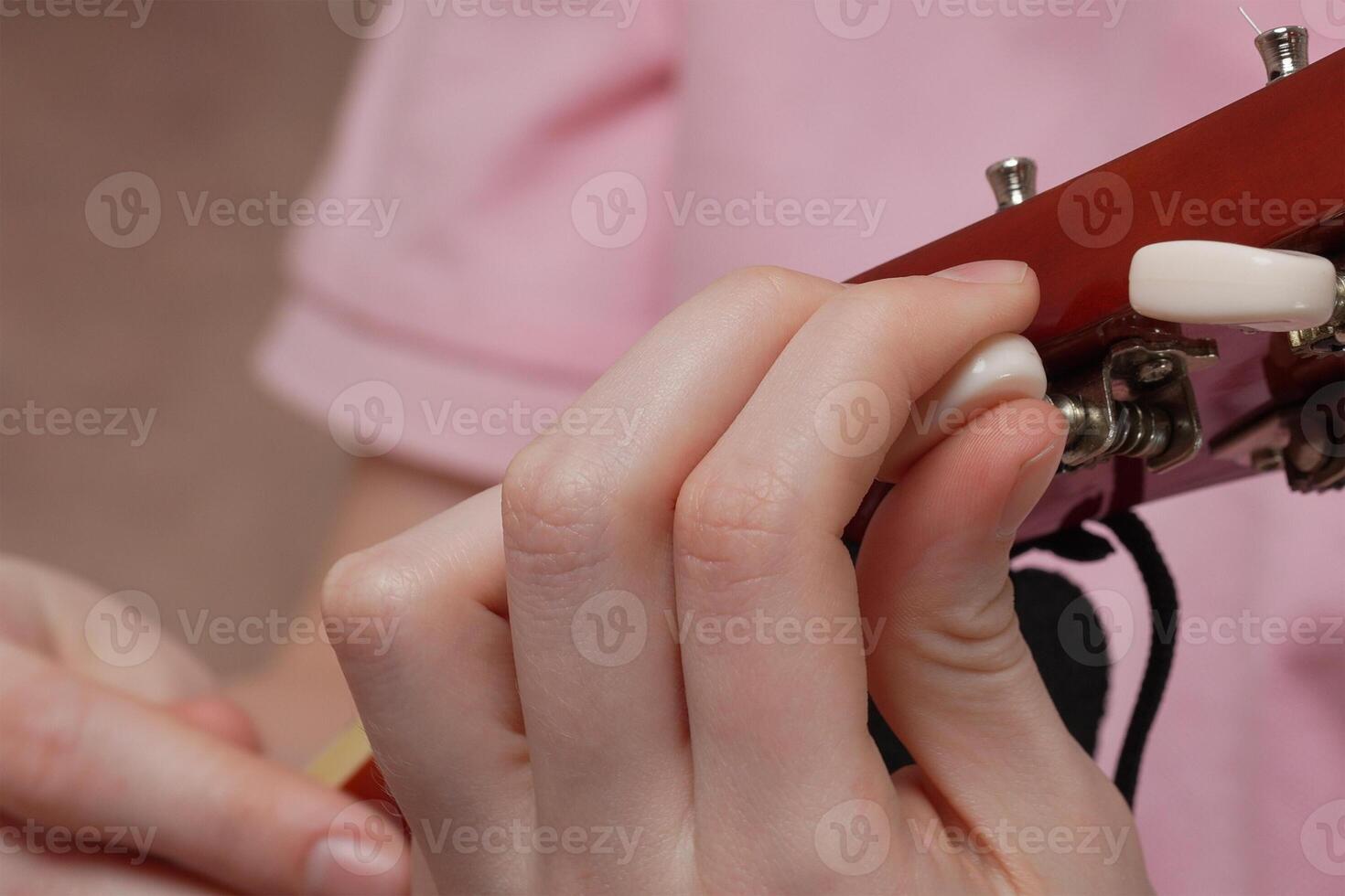Close-up of female fingers tuning acoustic guitar, tightening and loosening strings photo