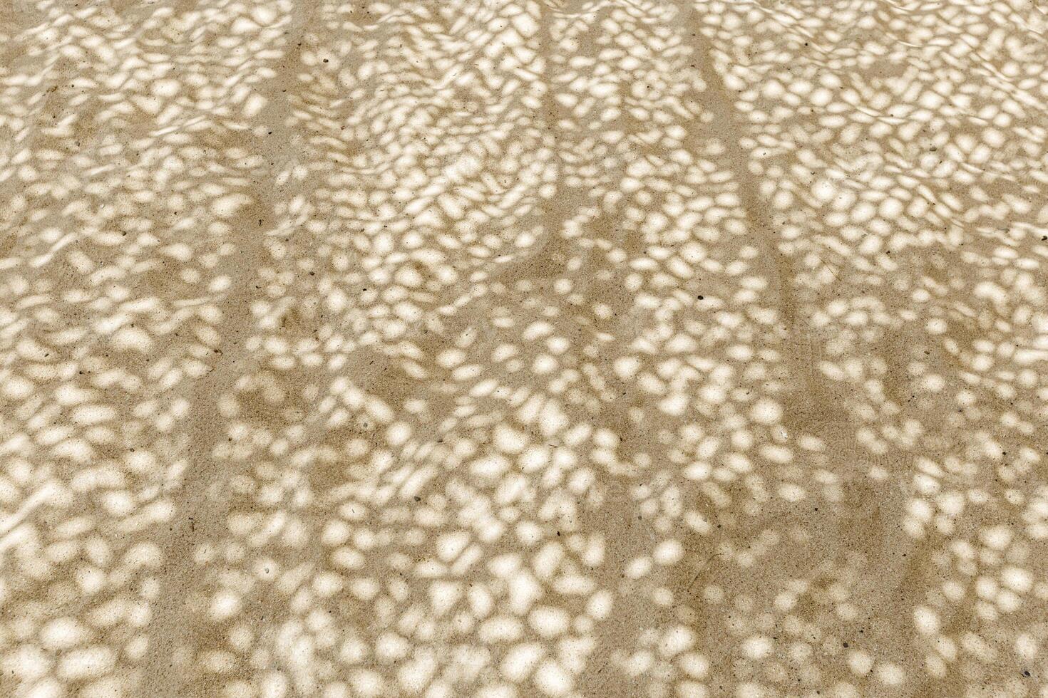 Shadow Patterns on Sand background, Natural light creates dappled shadow pattern on sandy beach. Summer time concept, nature backdrop. Top view texture photo