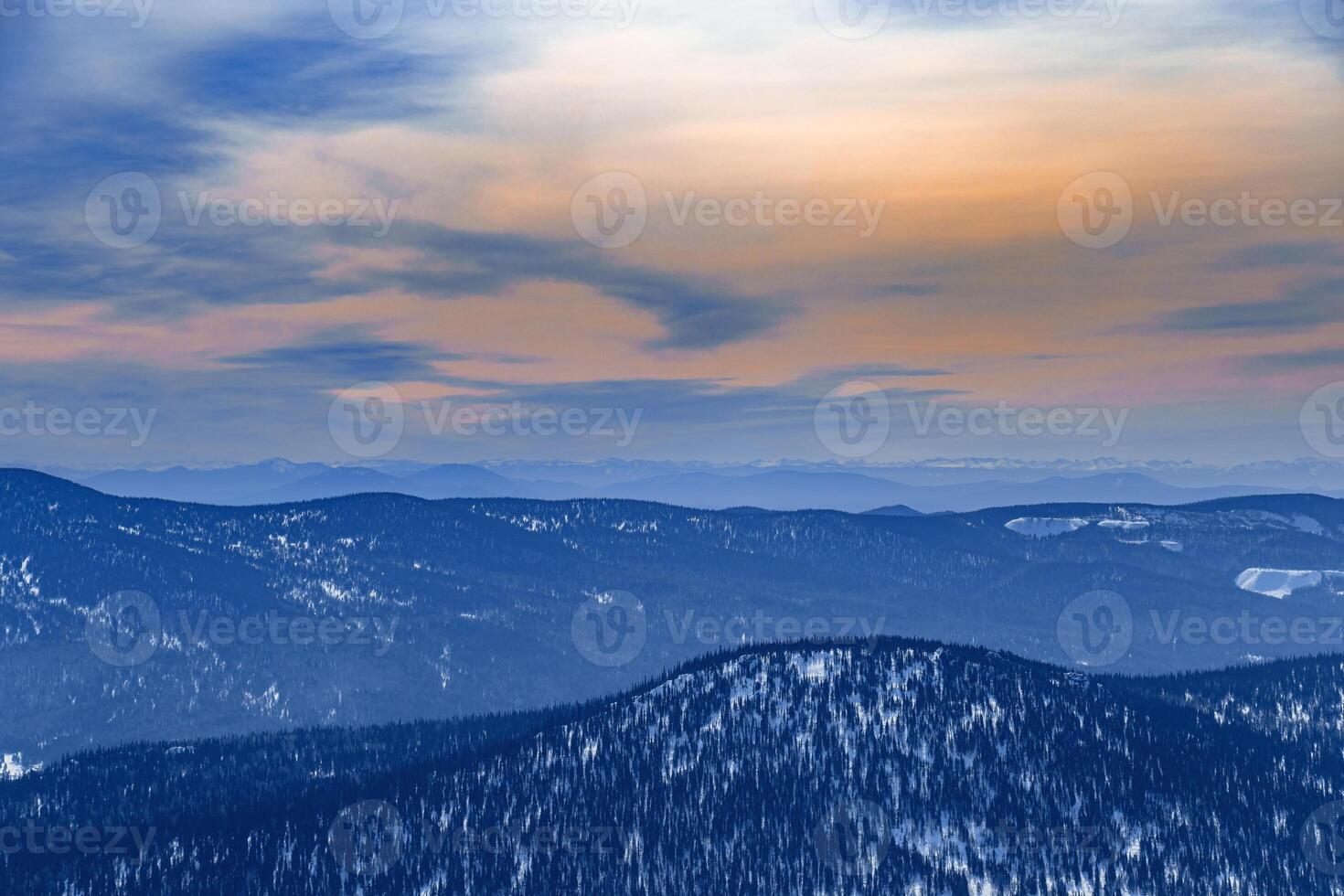 Winter nature panorama, sunset at mountains, picturesque view, aerial tonal perspective, range mountains and bright cloudy sky, hills covered forest and snow, beautiful landscape in Russia photo