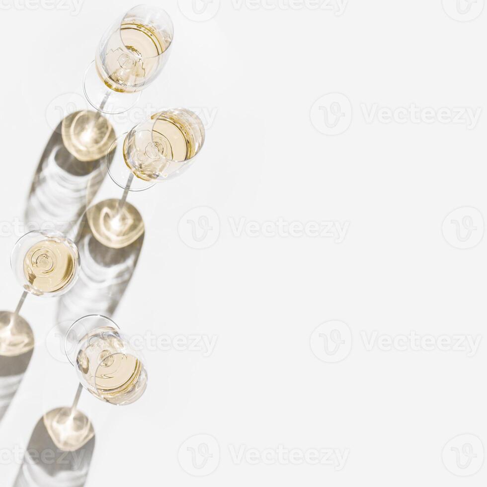 Many glasses of white wine, Aesthetic top view on white light background, minimal style flat lay. Wine glass at sunlight, sun shadows and shiny glare glass. Light alcohol drinks for party, events photo