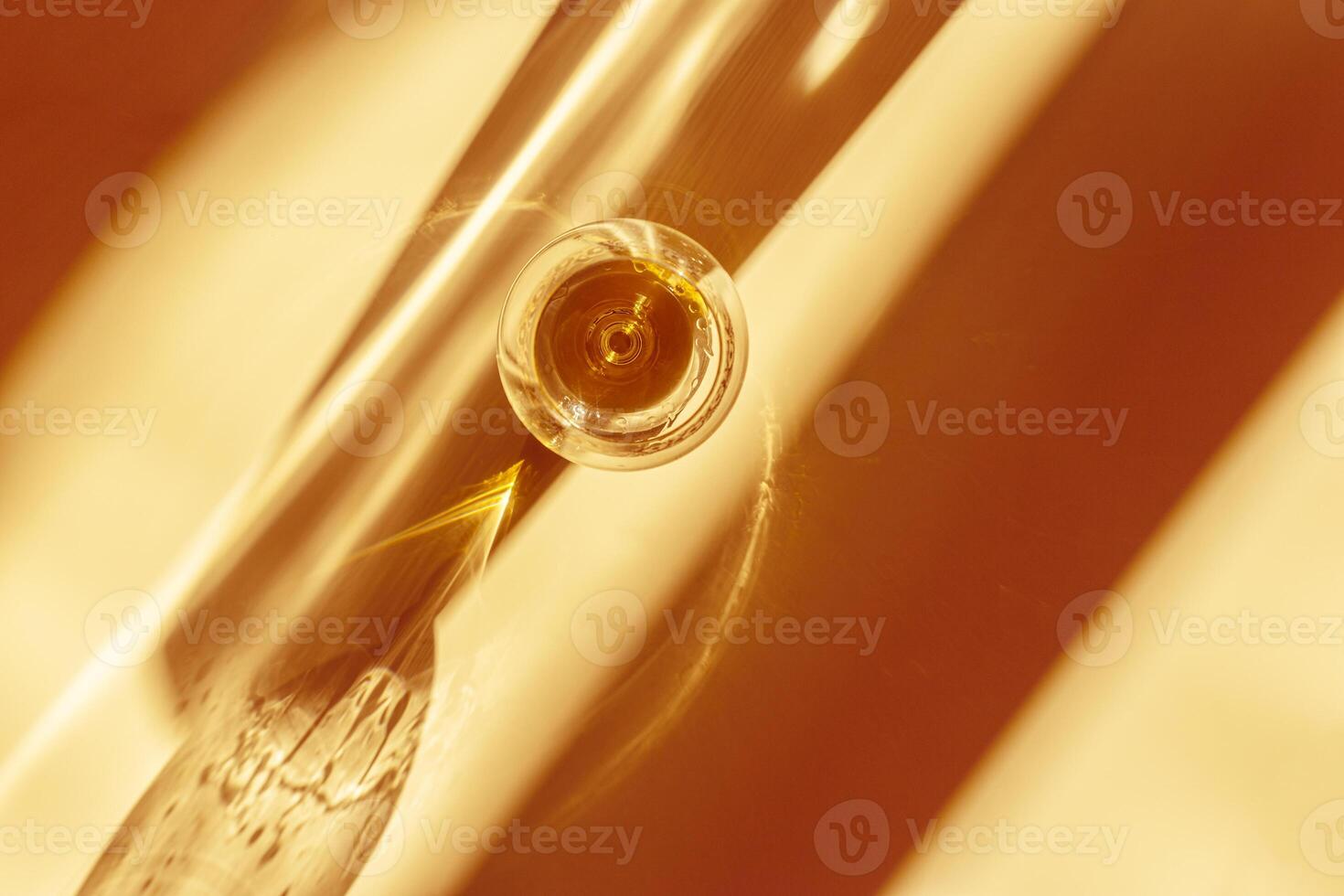 Sunlight still life with one glass of cognac, beige orange colored background with shadow and glare, light effect at sun on table. Minimal aesthetic toned photo with strong alcohol drink, view