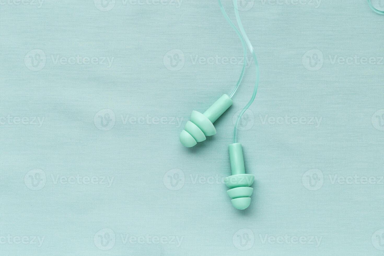 Reusable silicone mint earplugs on colored textile background, copy space. Against noise and water Ear plug on string, for swim, sleep, protect hear, aesthetic top view, minimal style photo