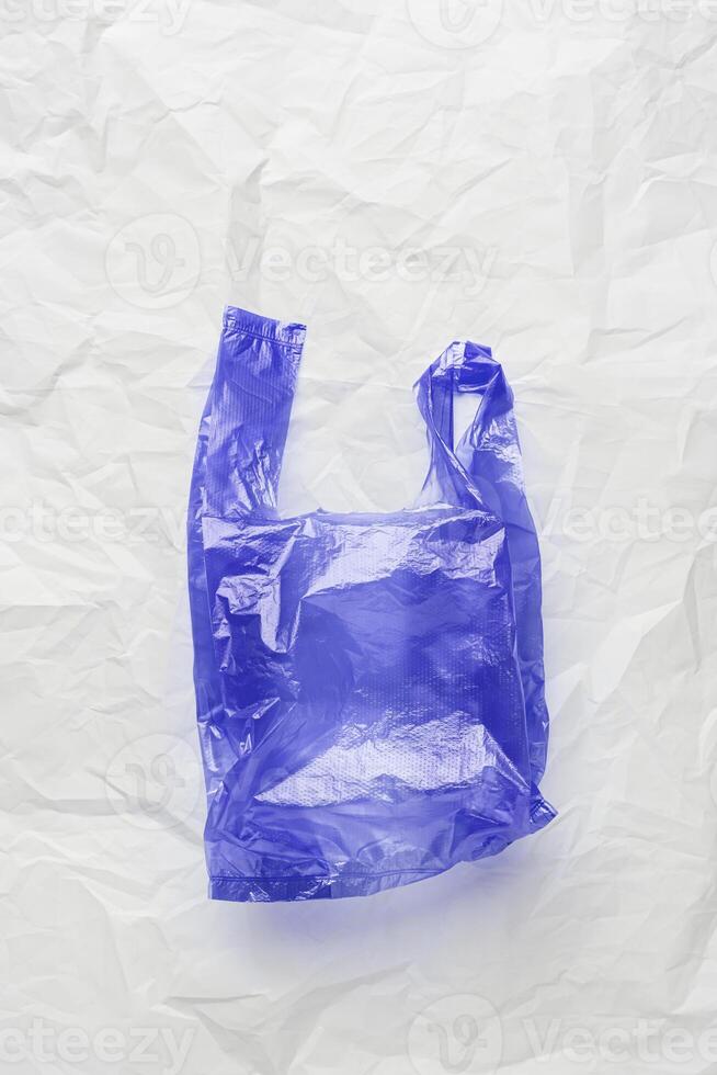 Plastic free concept, top view blue crumpled plastic bag crumpled on white wrinkled paper background. Disposable polythene packet for food. Eco trend minimal style photo, vertical photo, above photo