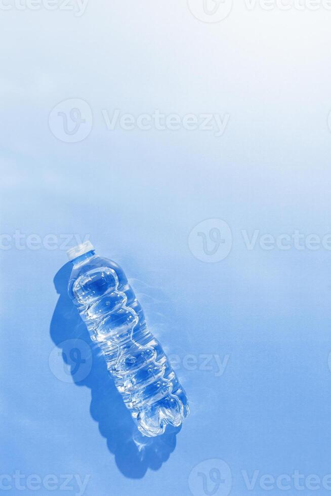 Plastic bottle water at sunlight with beautiful sun shadow on blue color background, copy space. Clean drinking water in bottle. Pollution, environmental protection concept. World water problem photo