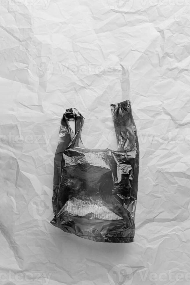 Plastic free concept, black and white, top view crumpled plastic bag crumpled on wrinkled paper background. Disposable polythene packet for food. Eco trend minimal style photo, monochrome photo