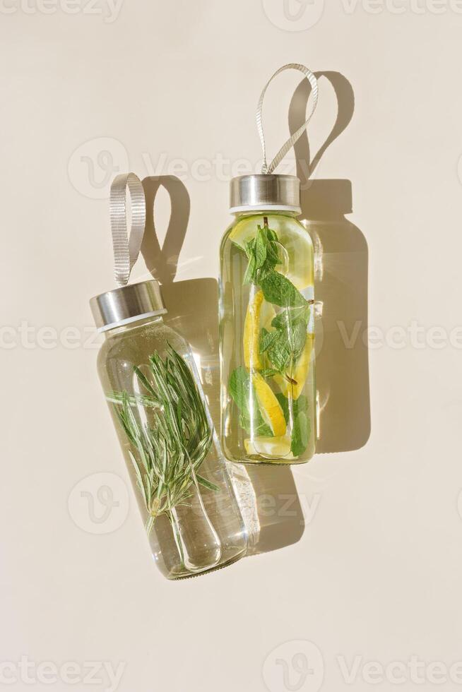 Glass bottle with lemon mint and herbs rosemary water drink detox at sunlight on beige table background, copy space. Natural Infused water Health drink. Aesthetic still life, refreshing drink photo