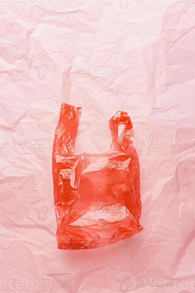 Plastic free concept, top view plastic bag crumpled on pink wrinkled paper background, copy space. Disposable polythene packet for food. Eco trend minimal style photo, red monochrome photo