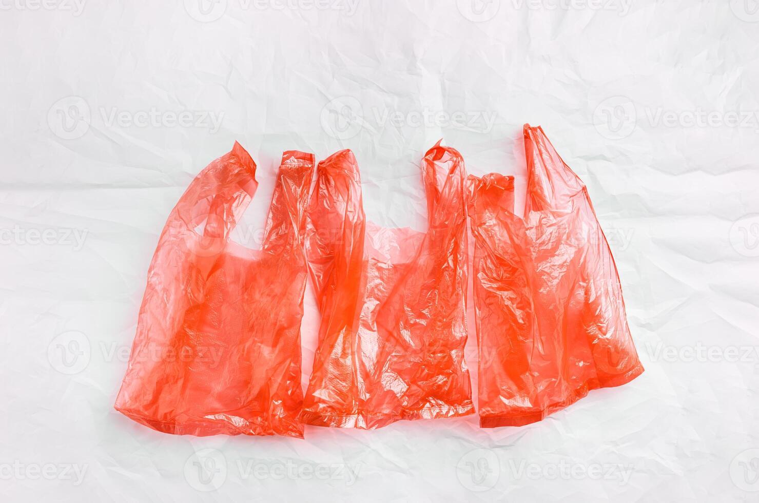 Red transparent plastic bags on white crumpled paper background, , conscious lifestyle concept, minimal style aesthetic image. Single-use plastic ban. Eco trend to reduce disposable plastics, top photo