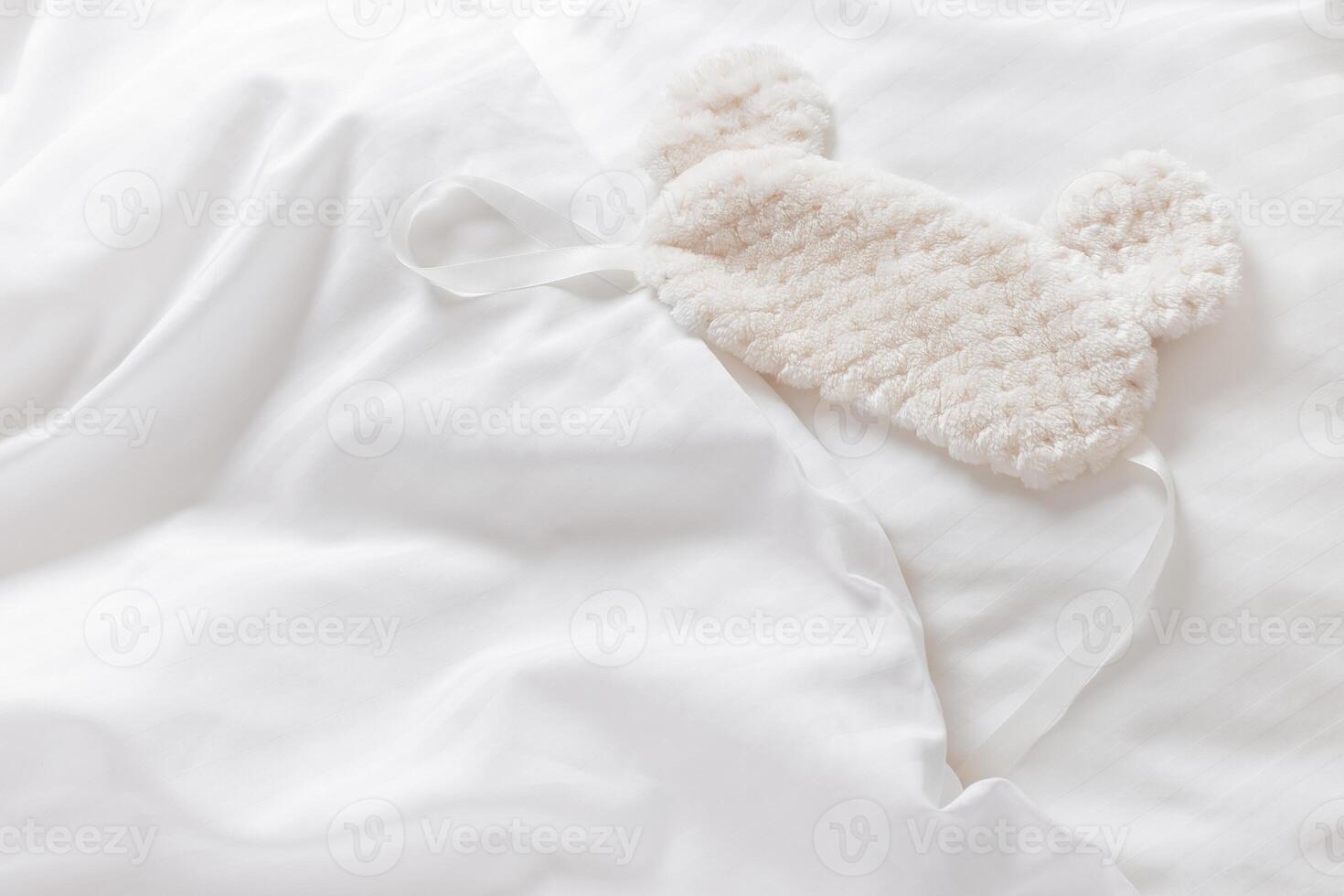 Sleep mask ofsoft nice fur on bed with white pillow and blankets bedclothes. Cozy life style home image. Fluffy eye cover mask for best sleep. Concept of home comfort, top view, flat lay photo