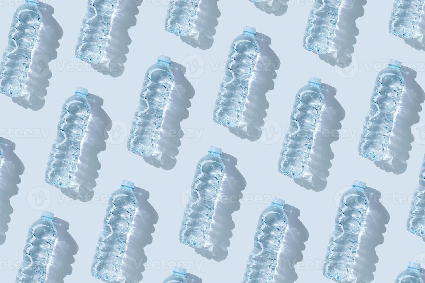 Pattern small plastic bottles with clean drinking water at sunlight, shadow on blue background. Full closed bottle water half litre. Pollution, plastic garbage, non-biodegradable packaging waste photo