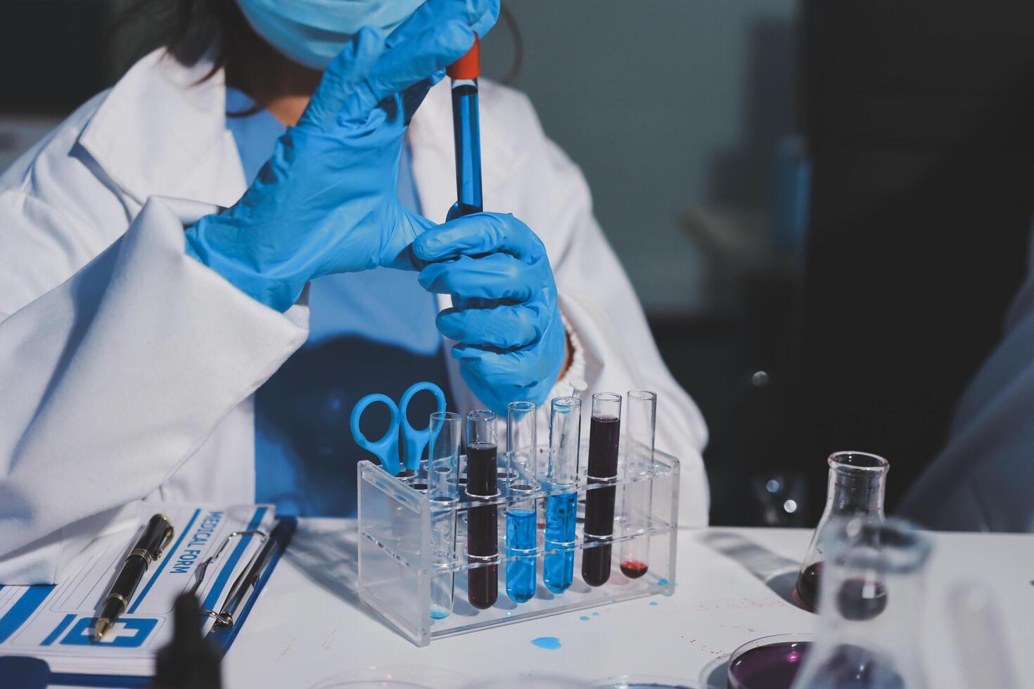 A person in a lab coat and gloves holding a test tube photo