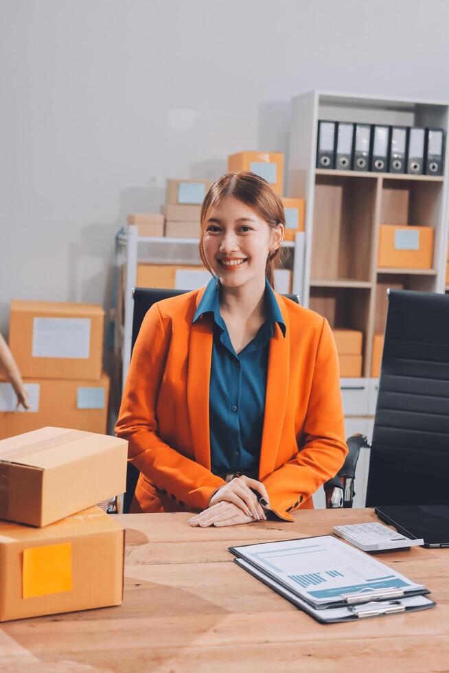 A woman in an orange jacket sitting at a desk with boxes photo