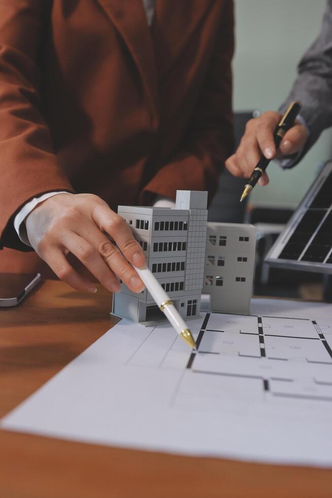 A man is holding a pen and pointing at a model of a building photo
