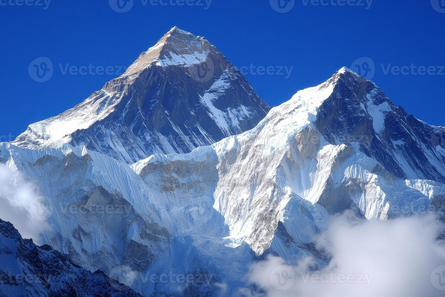 Two snow covered mountains with a blue sky in the background. The mountains are covered in snow and appear to be very tall photo