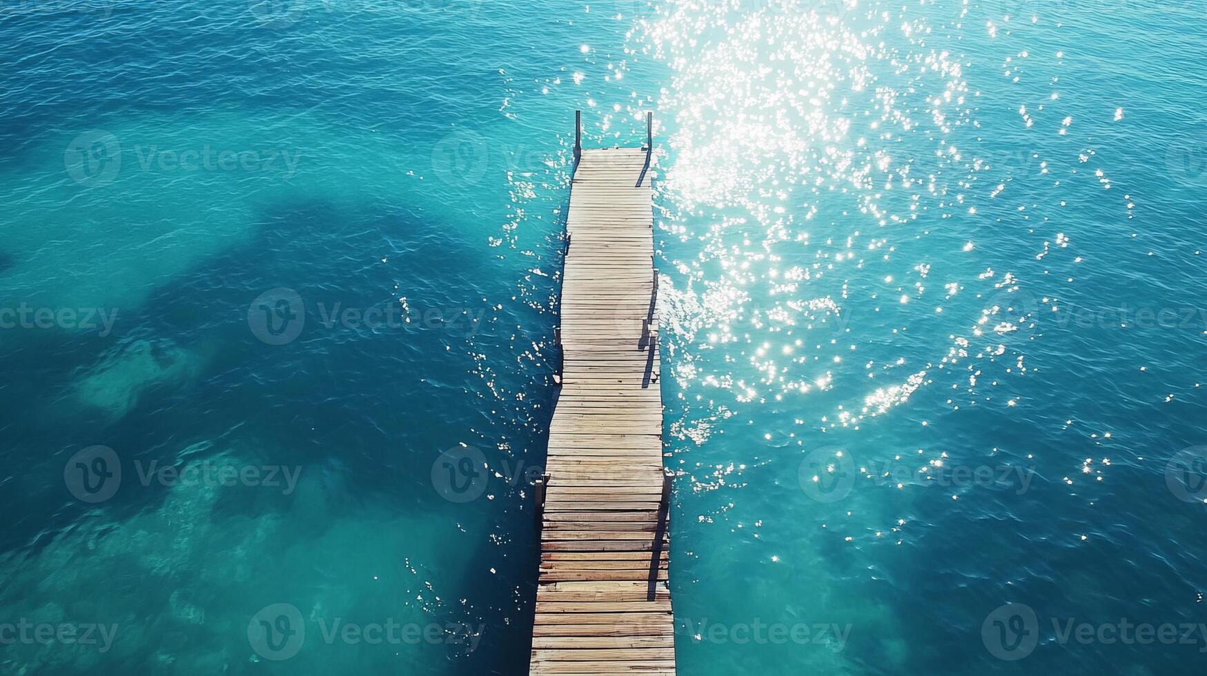 Stunning aerial shot of a wooden pier stretching into a vibrant turquoise sea, with sunlight creating a sparkling effect on the water. photo