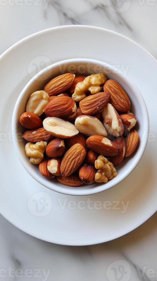 Bowl of nuts is on a white plate. The nuts include almonds, walnuts, and cashews photo