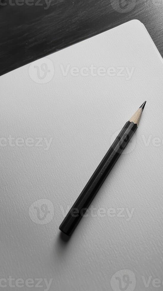 A black pencil resting on a blank white sheet, showcasing minimalist design and creative potential in a monochrome setting. photo