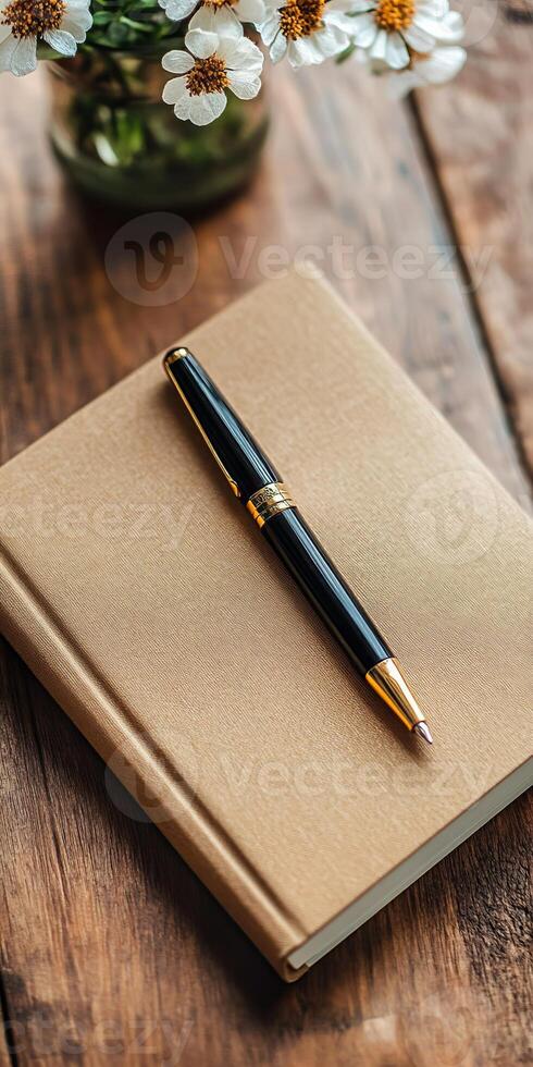 A sophisticated black fountain pen placed on a brown notebook, accompanied by a vase of daisies on a rustic wooden table. photo