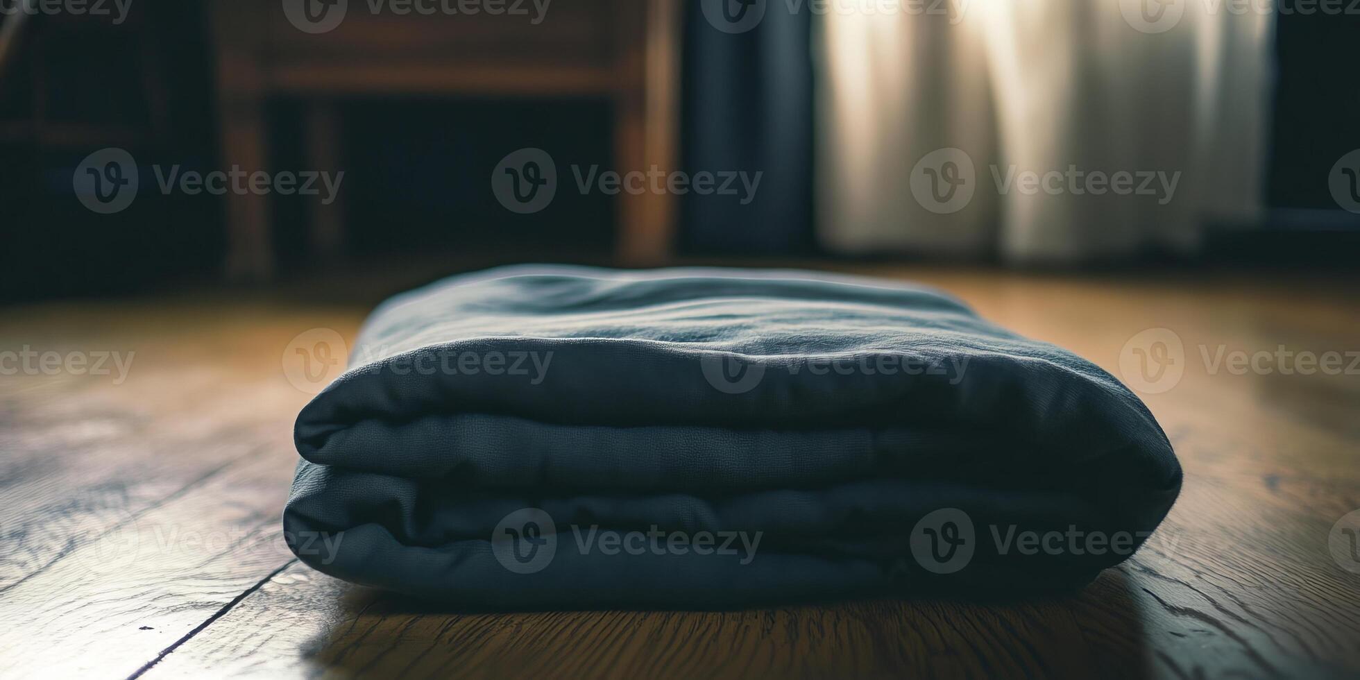 A neatly folded blanket on a wooden floor, illuminated by natural sunlight streaming through soft curtains. photo