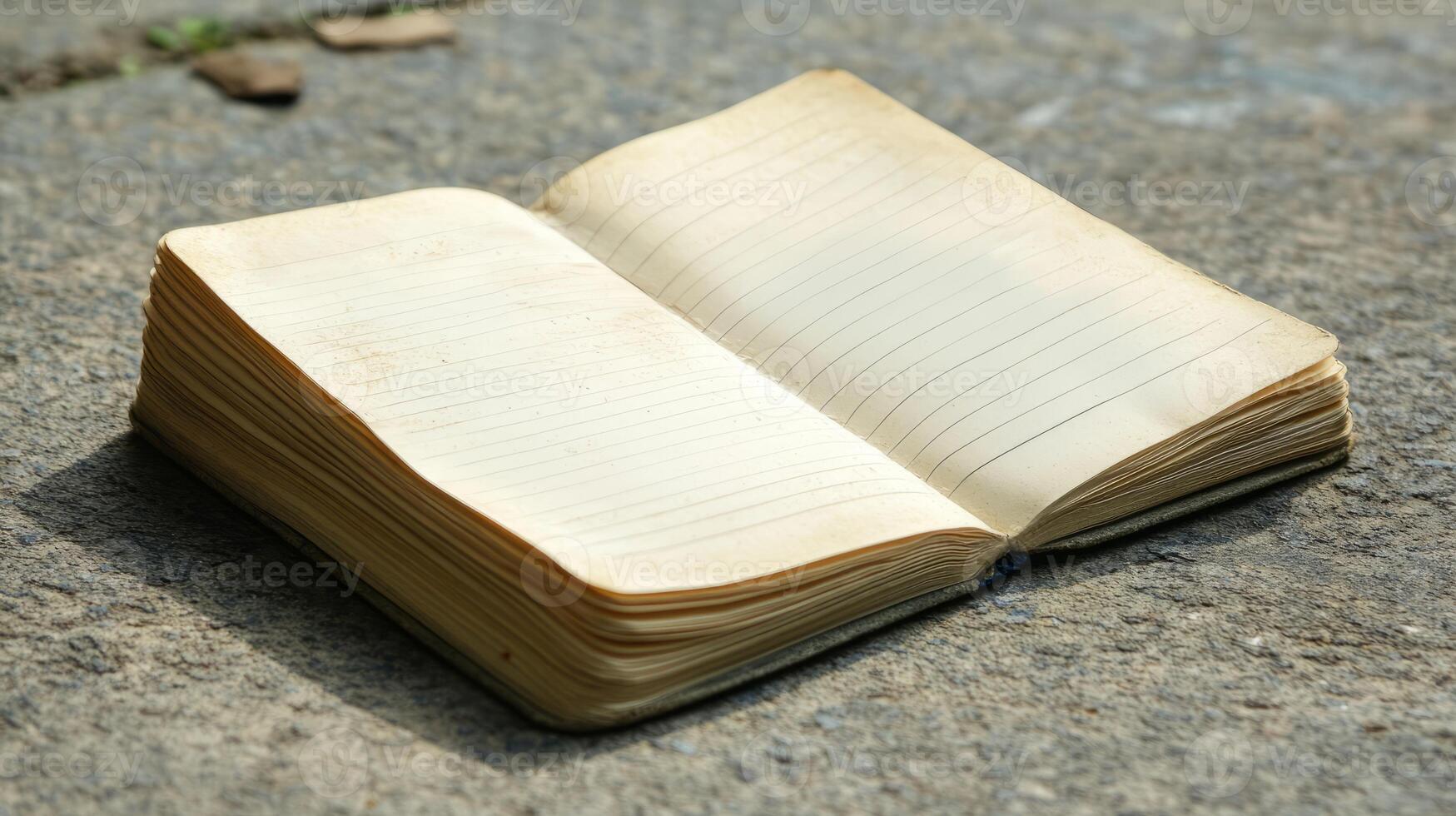 An open vintage notebook with lined pages on a rustic stone surface, ideal for writing or sketching in an outdoor setting. photo