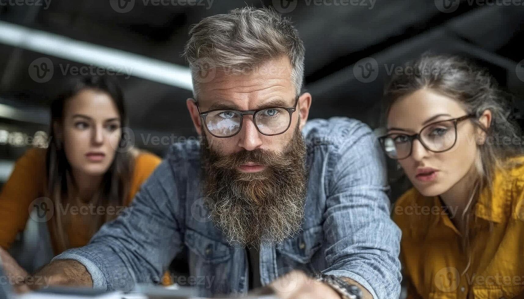 In a collaborative workspace, a diverse team of professionals, including a bearded man with glasses, gathers around a table, deeply engrossed in a project unfolding on a laptop screen, their photo