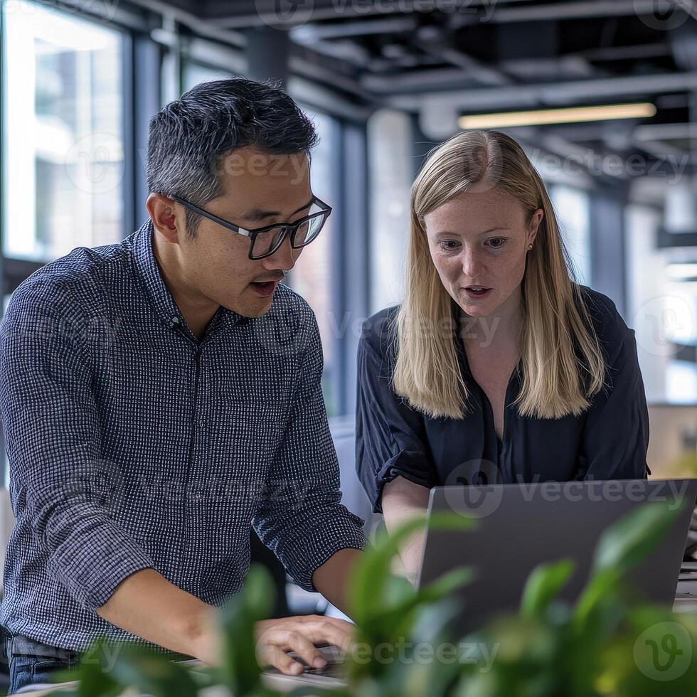 Two Colleagues Collaborating on a Laptop in a Modern Office Setting, Discussing Business Strategies and Analyzing Data, Focused on Achieving Project Goals with Teamwork and Communication, Utilizing photo