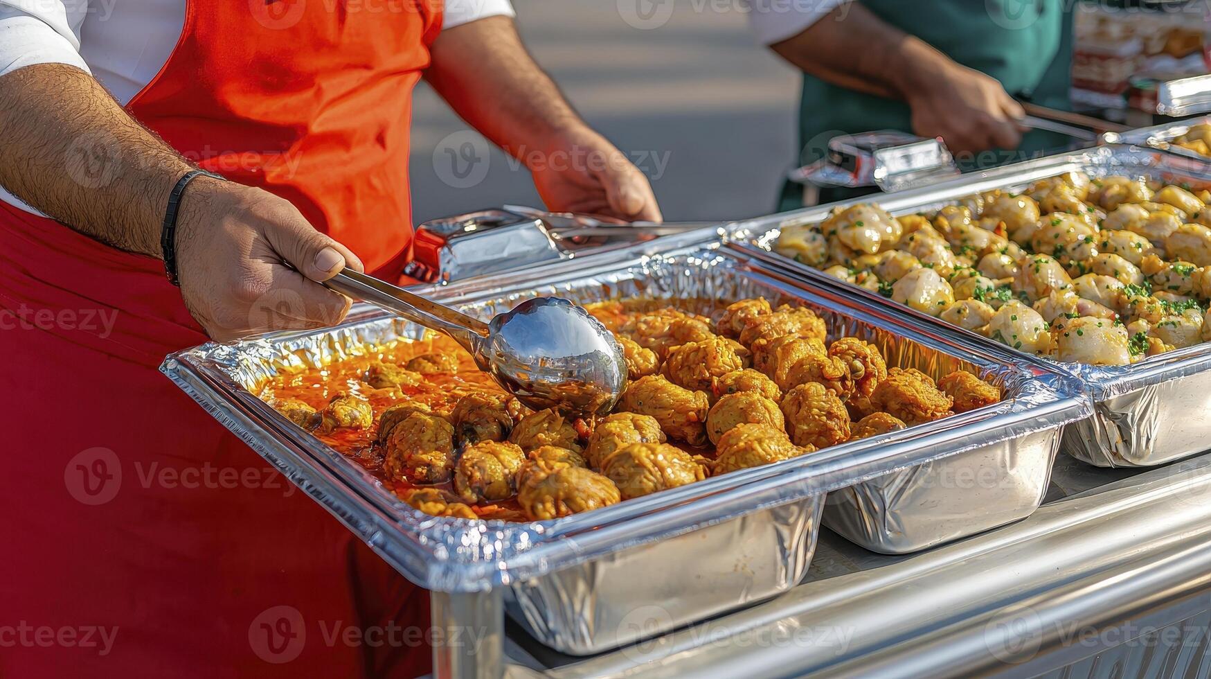 Delicious street food catering in an outdoor setting showcases a variety of flavorful dishes, including tender meatballs in savory sauces and golden, crispy potatoes, presented in aluminum trays photo