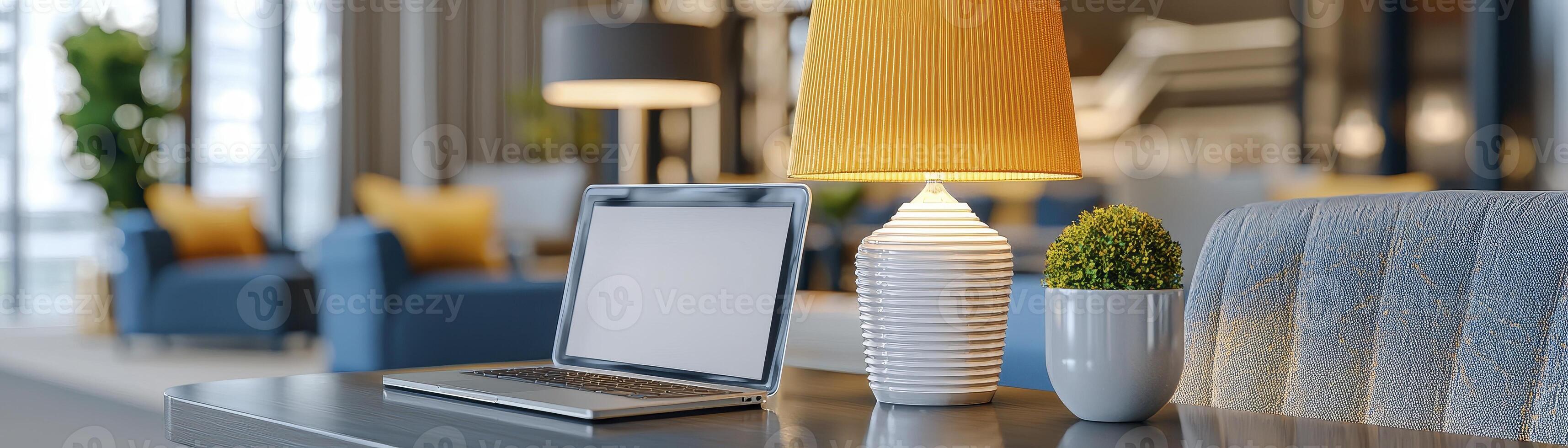 A contemporary workspace showcases a laptop with a pristine white screen, positioned beside a bright yellow lamp A decorative green plant adds a touch of nature to the scene, all set against a photo