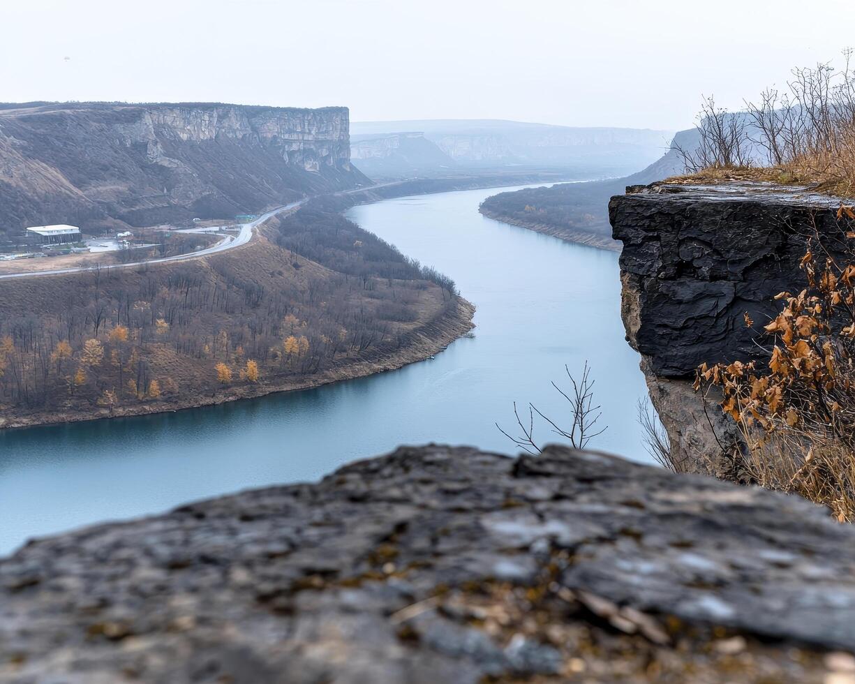 A serene river carves its path through the rugged landscape, painting a tableau of nature's artistry The tranquil waters, reflecting the sky's gentle hues, meander gracefully Towering cliffs stand photo