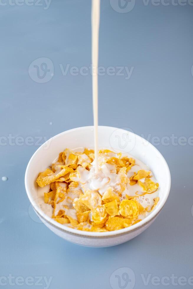 A close-up of fresh milk being poured into a bowl of golden cornflakes photo