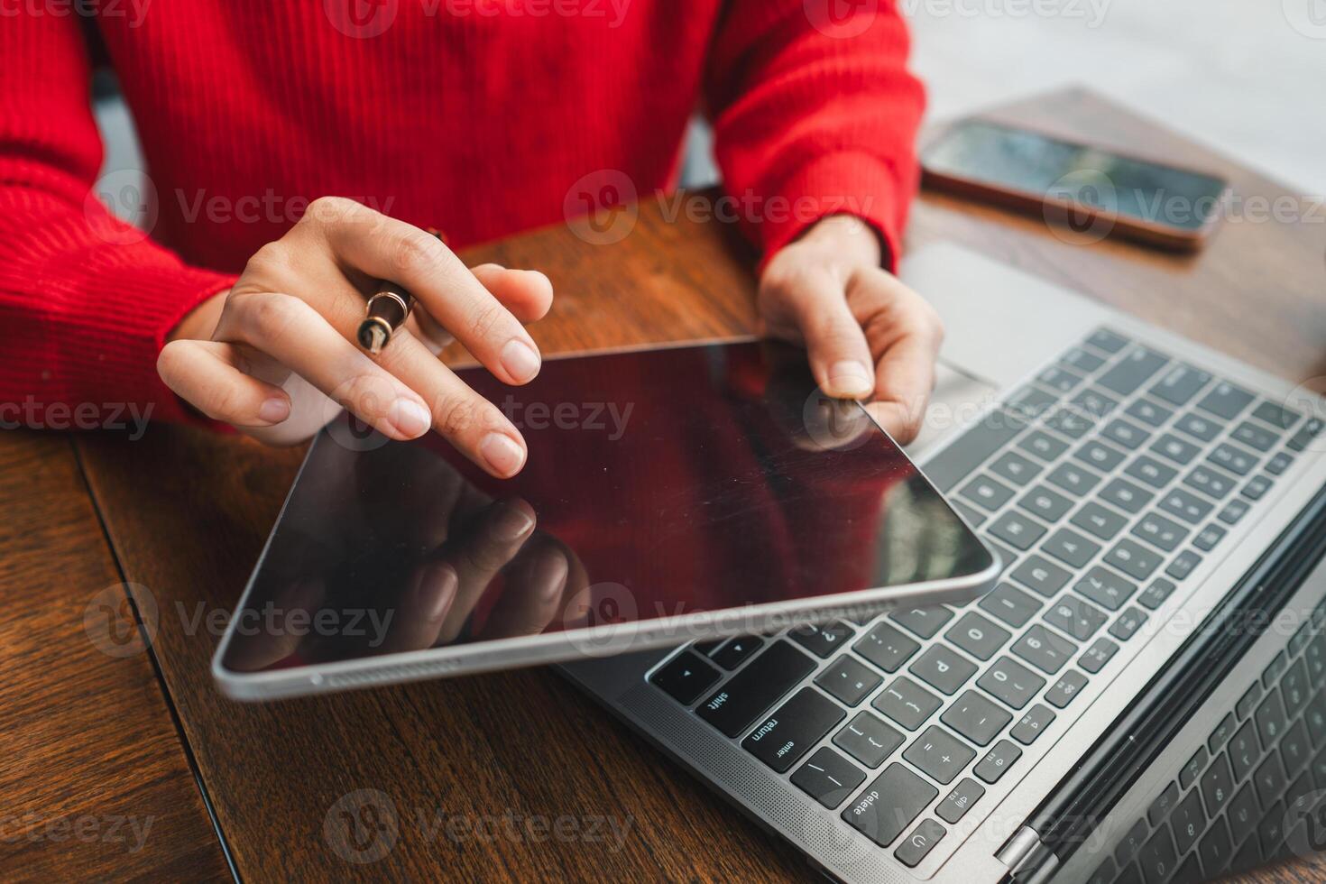 Hands interacting with a tablet next to a laptop on a wooden desk, showcasing modern technology in a casual setting. photo