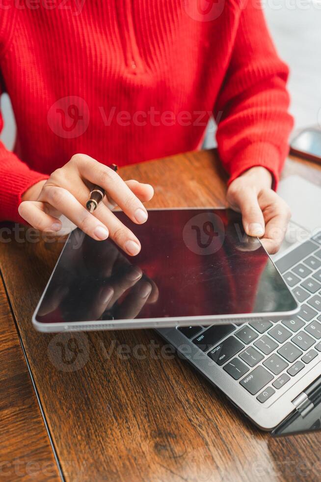 Close-up of hands holding a tablet and using a laptop, showcasing modern technology in a casual environment. photo