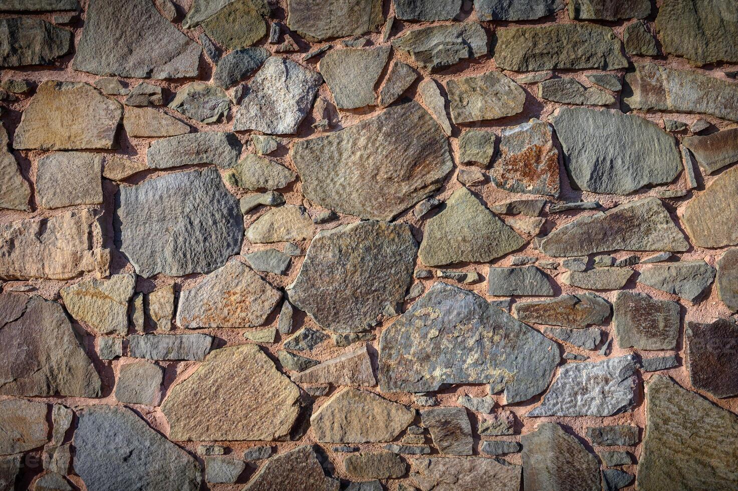 Textured stone wall showcasing natural hues and shapes from centuries of craftsmanship in a rustic setting photo