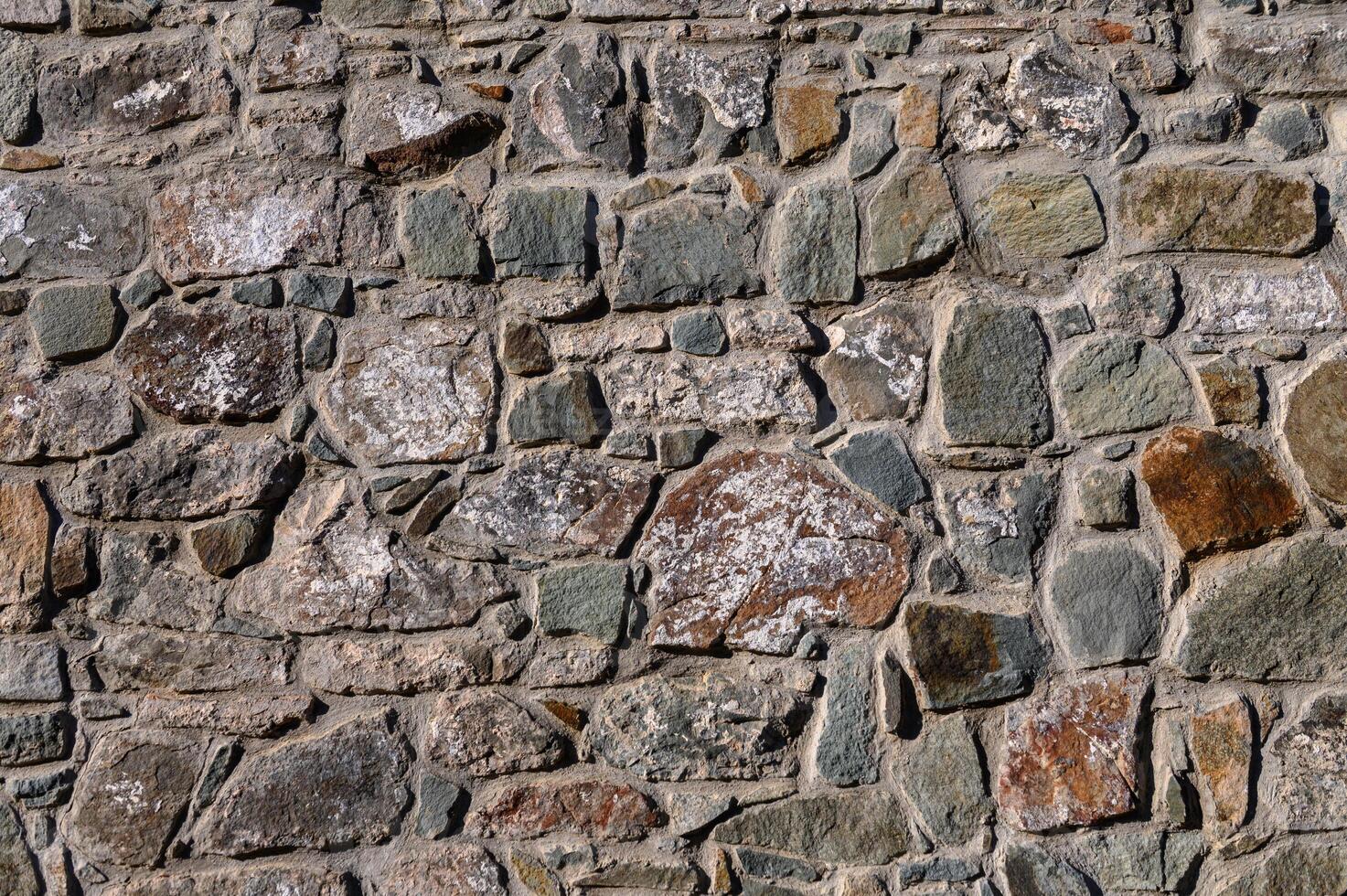 Weathered stone wall showcasing unique textures and colors in a sunlit rustic setting photo