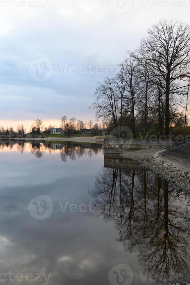 Calm reflections at dusk by the serene lakeside with trees and soft sunset hues photo