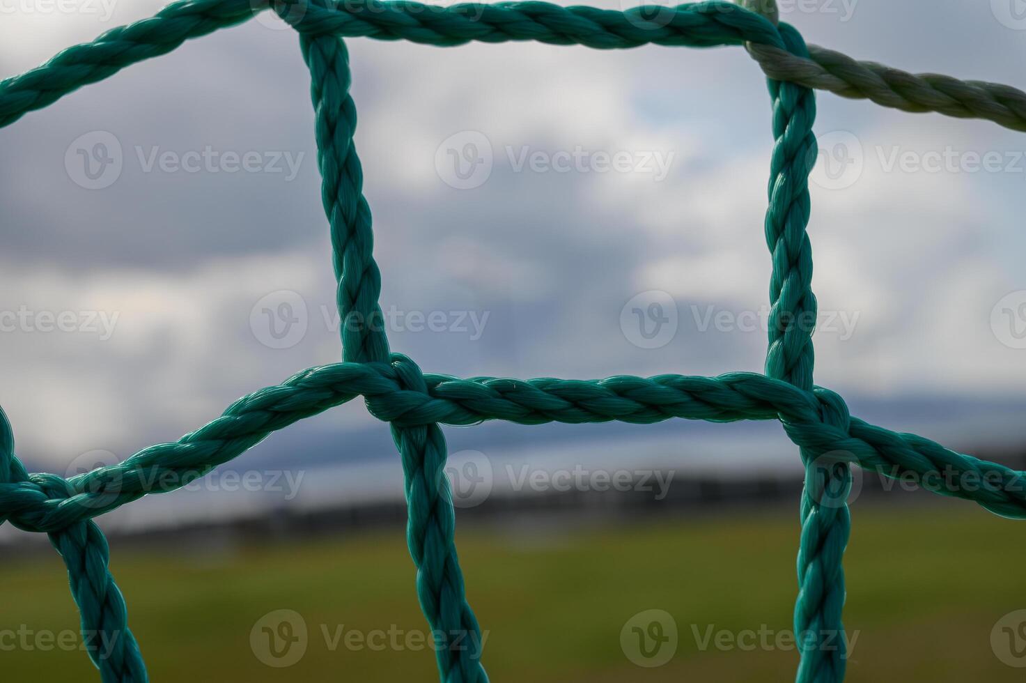 Vivid turquoise netting frames a blurred landscape under an expansive cloudy sky in a serene outdoor setting photo