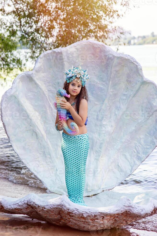 A smiling little girl in a mermaid costume in a large seashell, photo