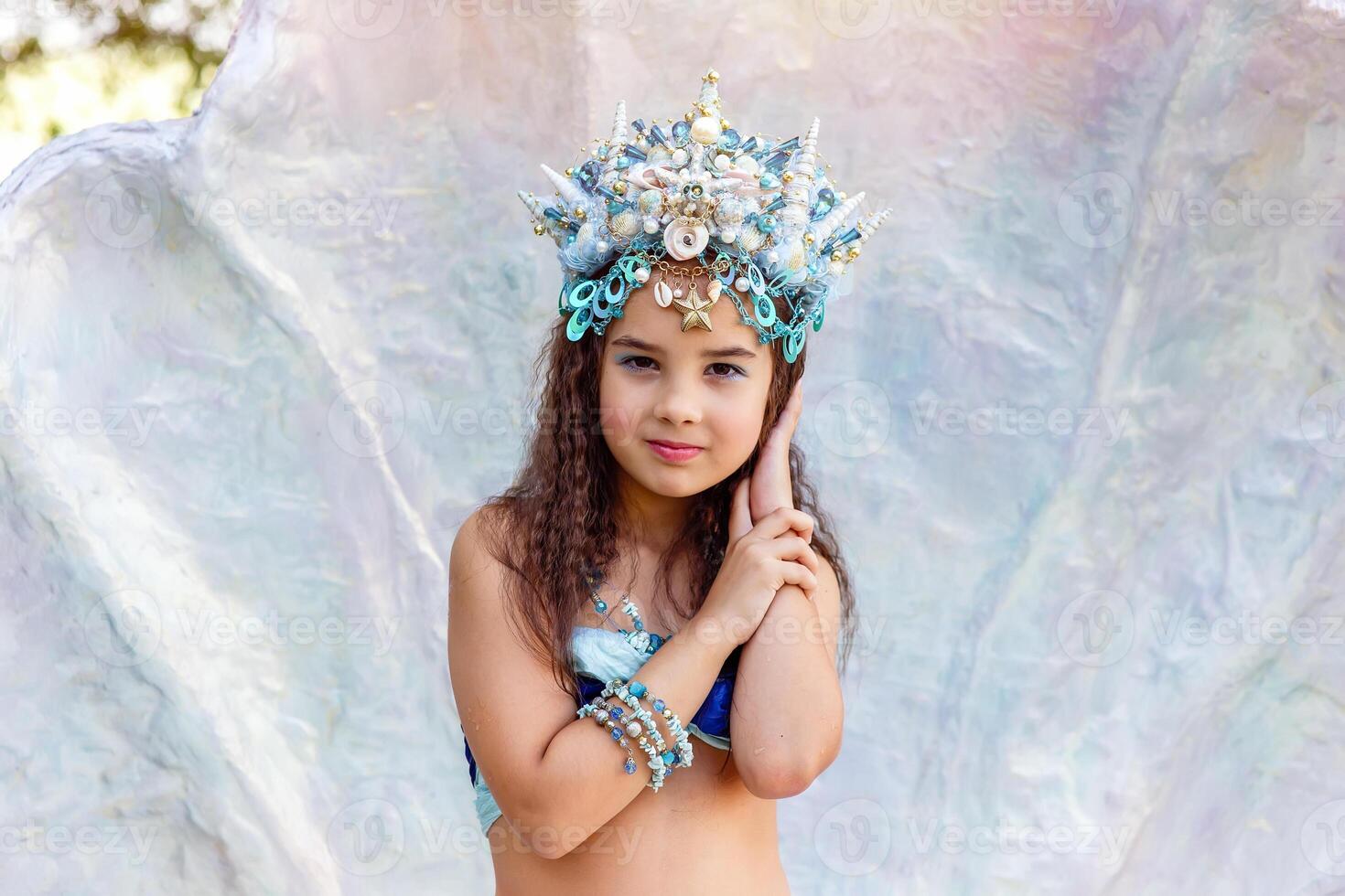 A beautiful little girl in a crown and mermaid costume in a large seashell photo